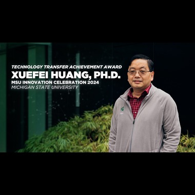 Xuefei Huang in gray sweater and red flannel standing in front of greenery.