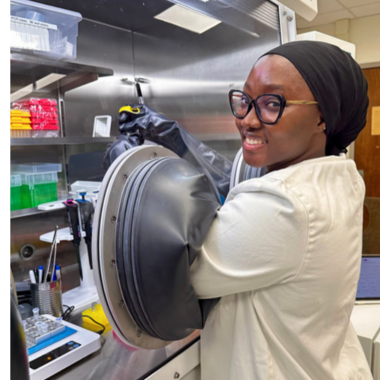 Shukurah Anas in lab coat and gloves