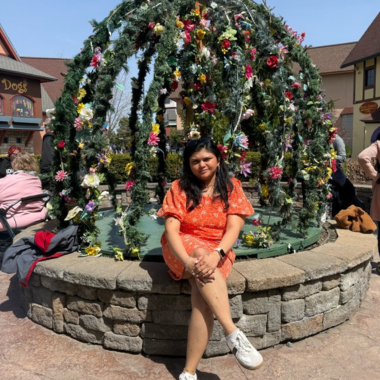 Deepika Davuluri sitting for a picture in an orange dress