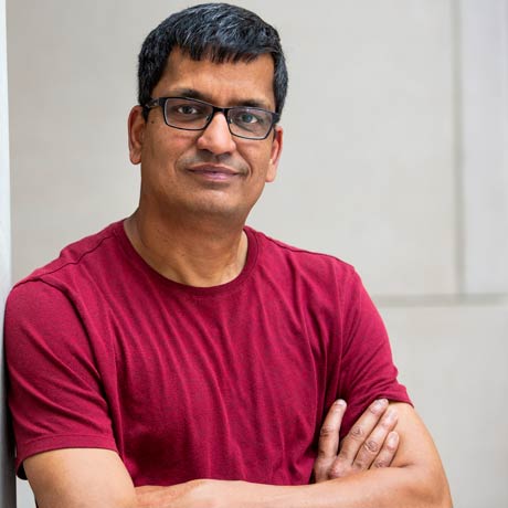 Rajendar Deora poses for a headshot with arms folded, wearing a red shirt.
