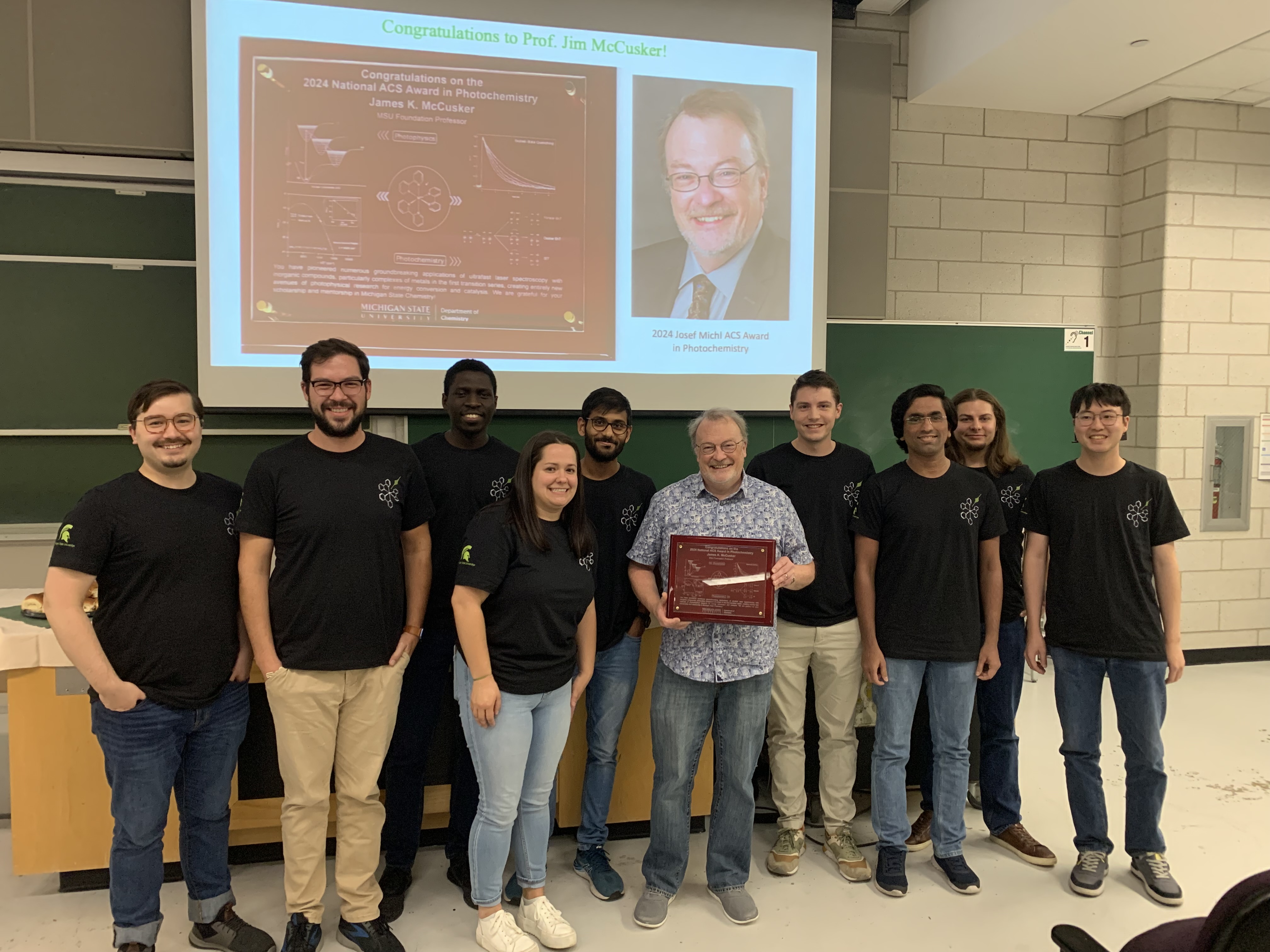 Professor James K. McCuskers poses with lab members and a plaque commemorating his Josef Michl ACS Award in Photochemistry.